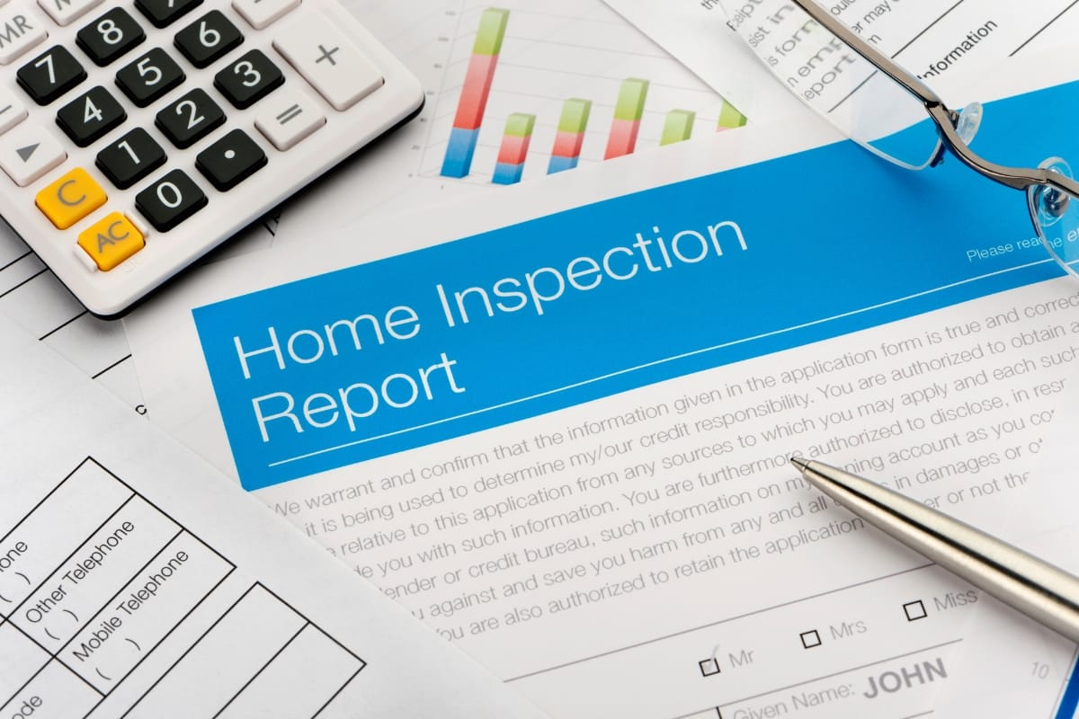 Close-up of a home inspection report on a table, surrounded by a calculator, charts, eyeglasses, and a pen. An HVAC system note stands out in the real estate inspection details, hinting at essential upgrades.