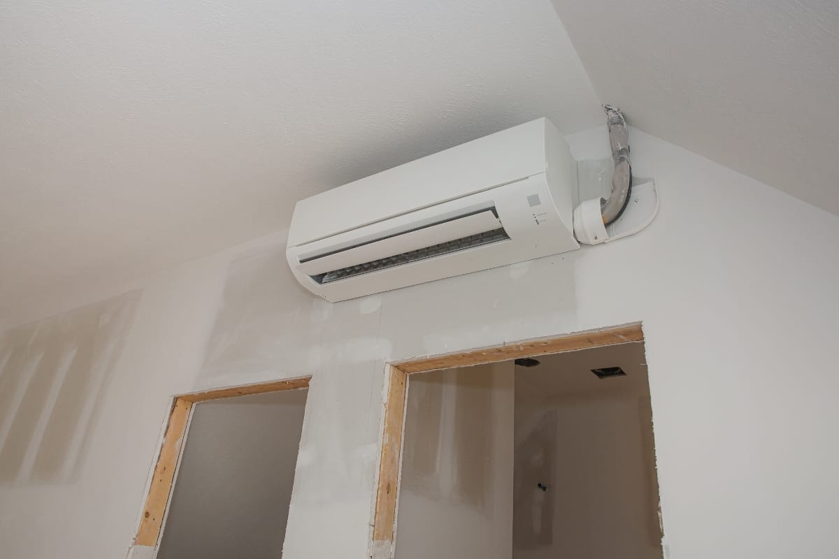 A wall-mounted air conditioning unit, a popular choice among various types of HVAC systems, is installed above two doorways in a room still under construction, complete with exposed drywall and unfinished surfaces.