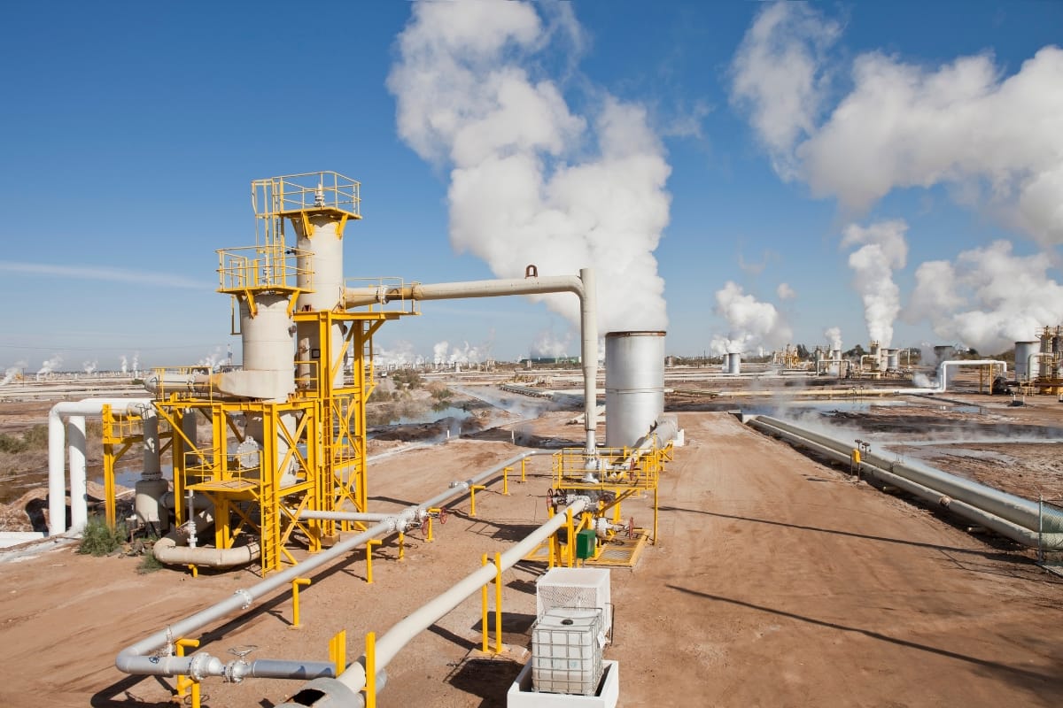 An industrial facility with yellow structures and pipes emitting steam showcases various types of HVAC systems in a vast, arid landscape under a clear blue sky.