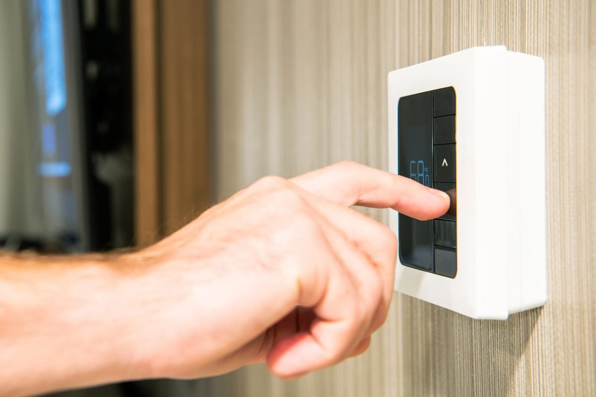 A hand adjusts a wall-mounted digital thermostat, optimizing comfort across various types of HVAC systems.