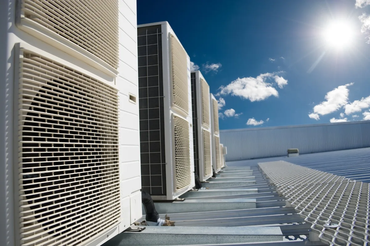 A row of large air conditioning units sits on a rooftop under a clear blue sky with bright sunlight, highlighting the need for environmental conservation efforts to balance modern comforts with sustainability.