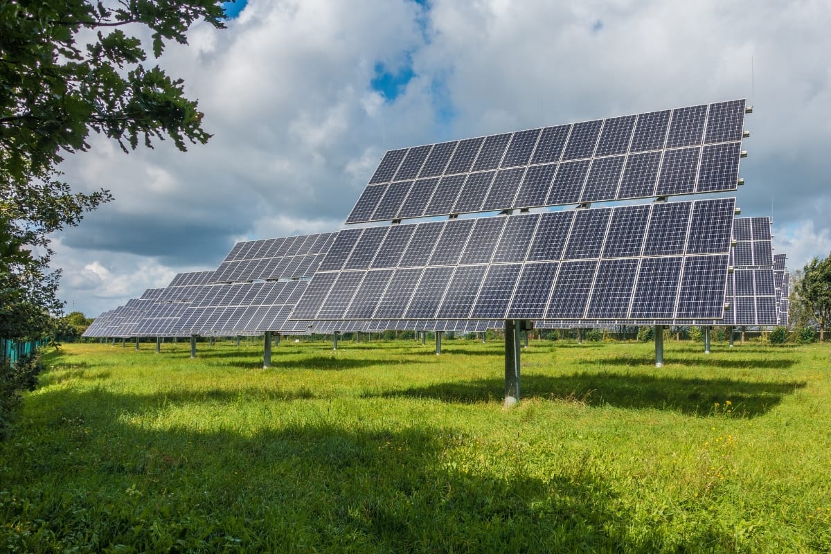 Rows of large solar panels mounted on metal supports are placed in a grassy field under a partly cloudy sky, embodying a commitment to environmental conservation.