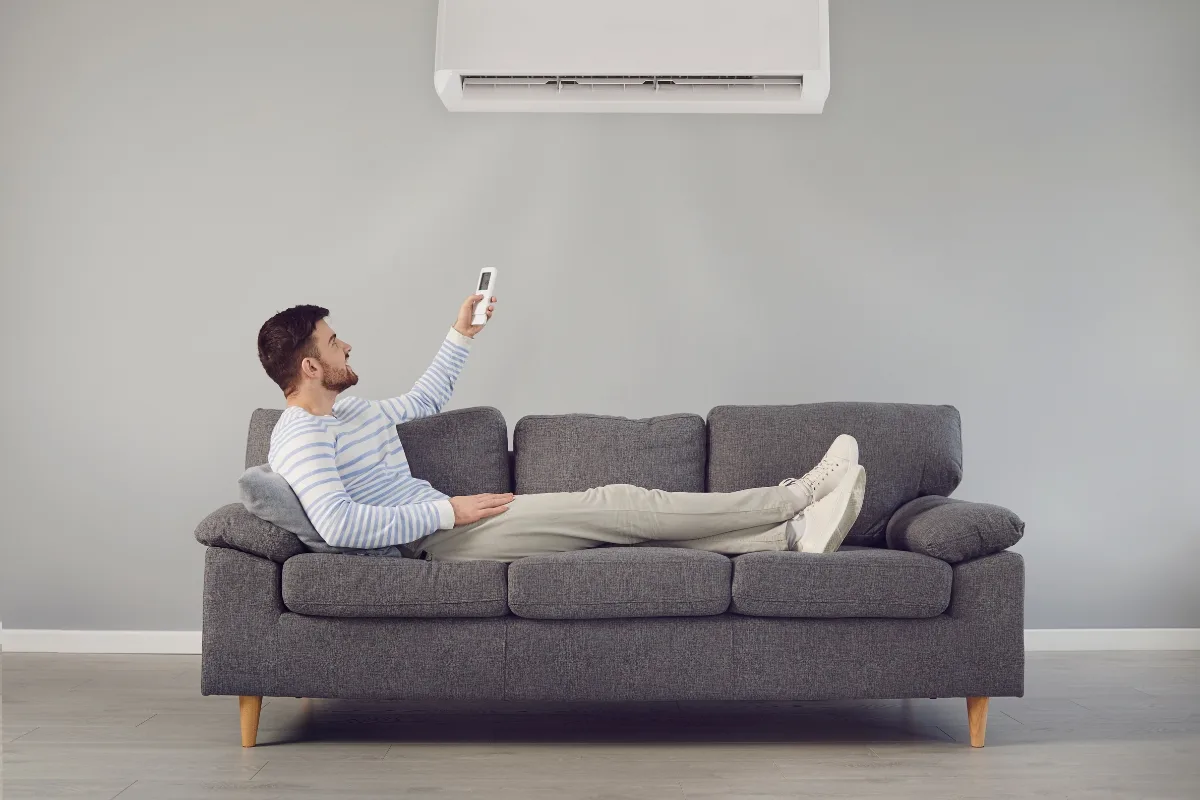A man in Holly Springs relaxes on a gray sofa, effortlessly adjusting his AC with a remote control in his modern living room, having recently resolved some minor AC problems.