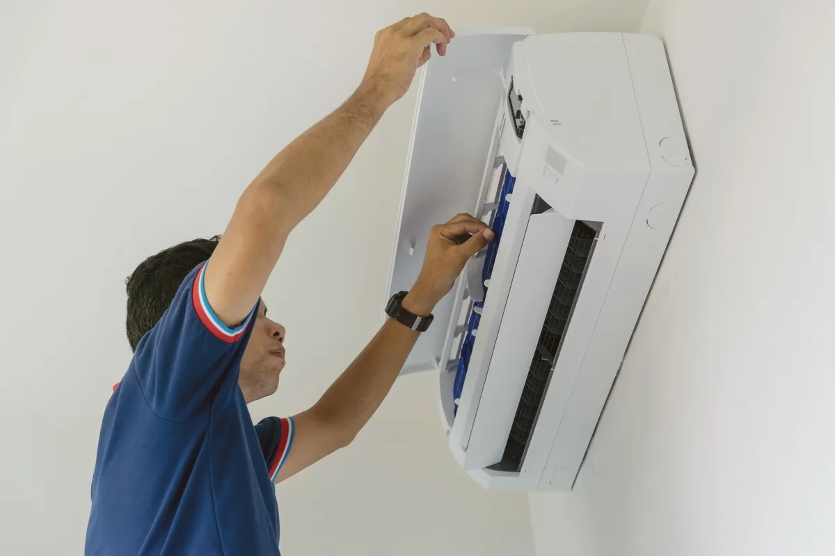 A person in a blue shirt is addressing AC problems by opening the front panel of a wall-mounted air conditioning unit, possibly for maintenance or repair, right in Holly Springs.