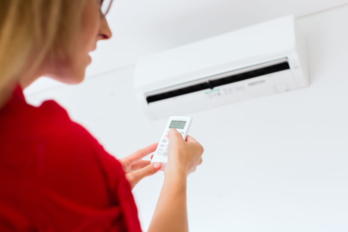A person in a red shirt uses a remote control to operate one of the best air conditioners, which is mounted on the wall.