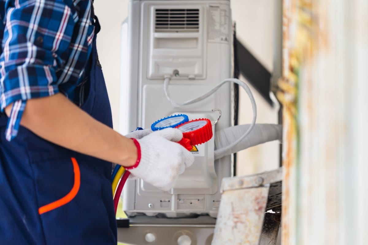 A technician in gloves uses a manifold gauge set to check or repair an outdoor air conditioning unit during an emergency AC repair.