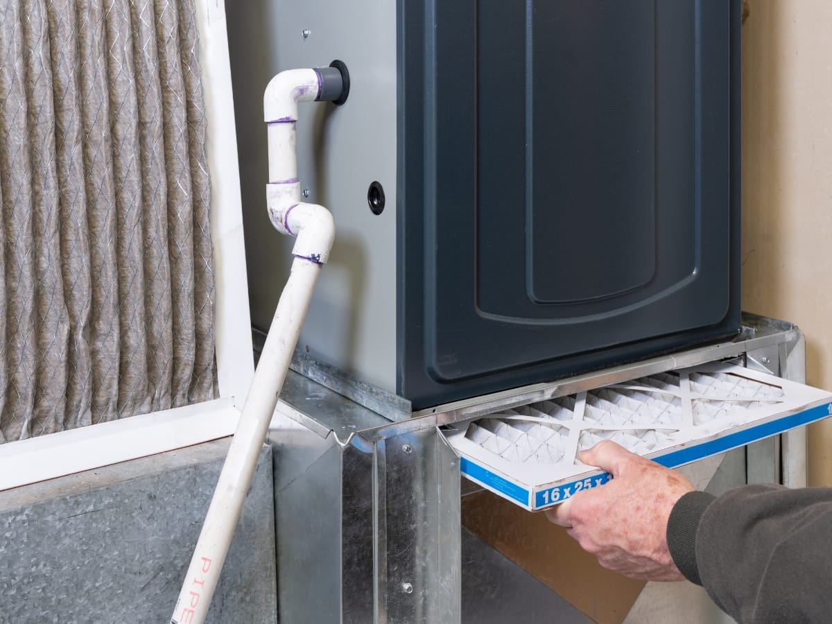 A person replaces a dirty air filter with a clean one in a residential HVAC furnace system as part of essential Fall HVAC Maintenance.