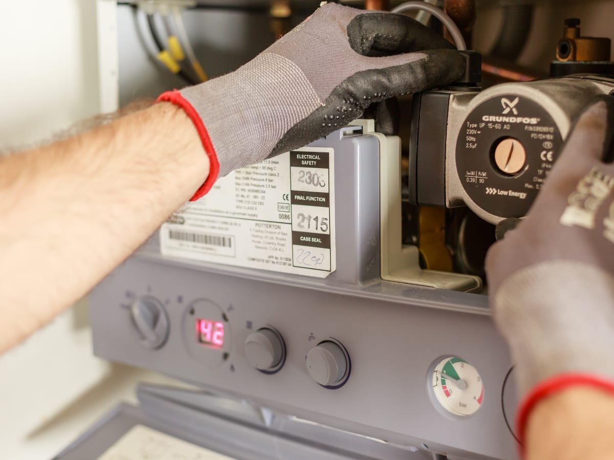 A person wearing gloves is adjusting controls inside a boiler or heating system panel, with digital and analog displays visible—typical work during a Dallas Furnace Repair.