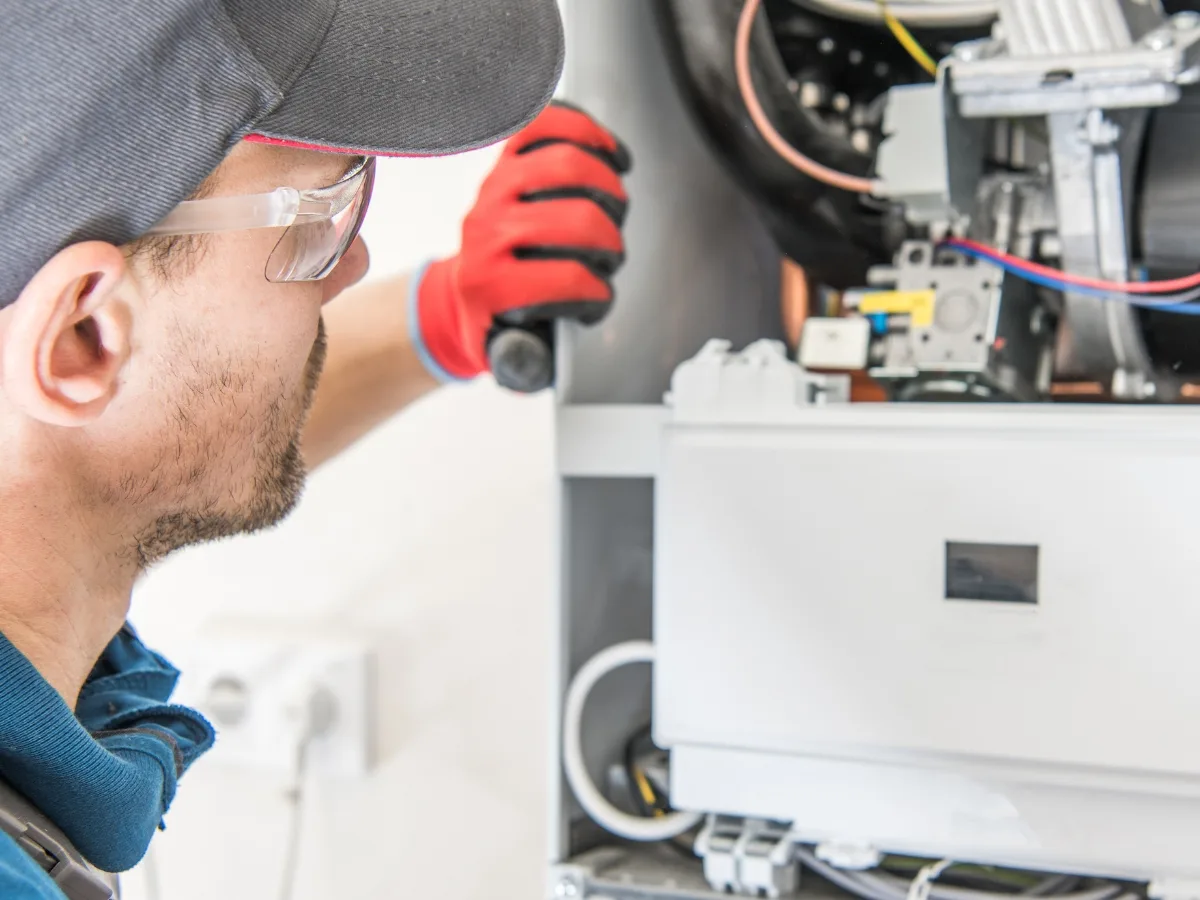 A technician wearing safety glasses and red gloves inspects or repairs the internal components of a household gas boiler, demonstrating the precision and care typical of Dallas Furnace Repair professionals.