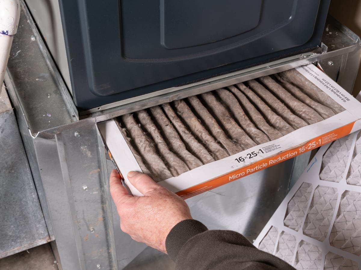 A person is removing a dirty, used air filter from a furnace for replacement—a common maintenance step to prevent Top Heating Problems.