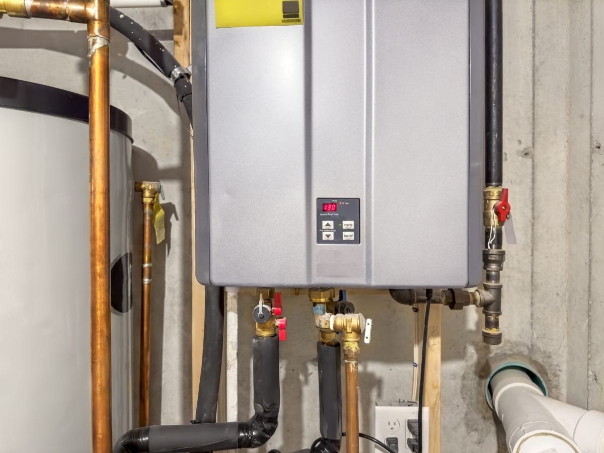 A modern tankless water heater is mounted on a basement wall, with pipes and a digital display visible—a reminder of the importance of regular maintenance like an annual furnace inspection for efficient home heating.