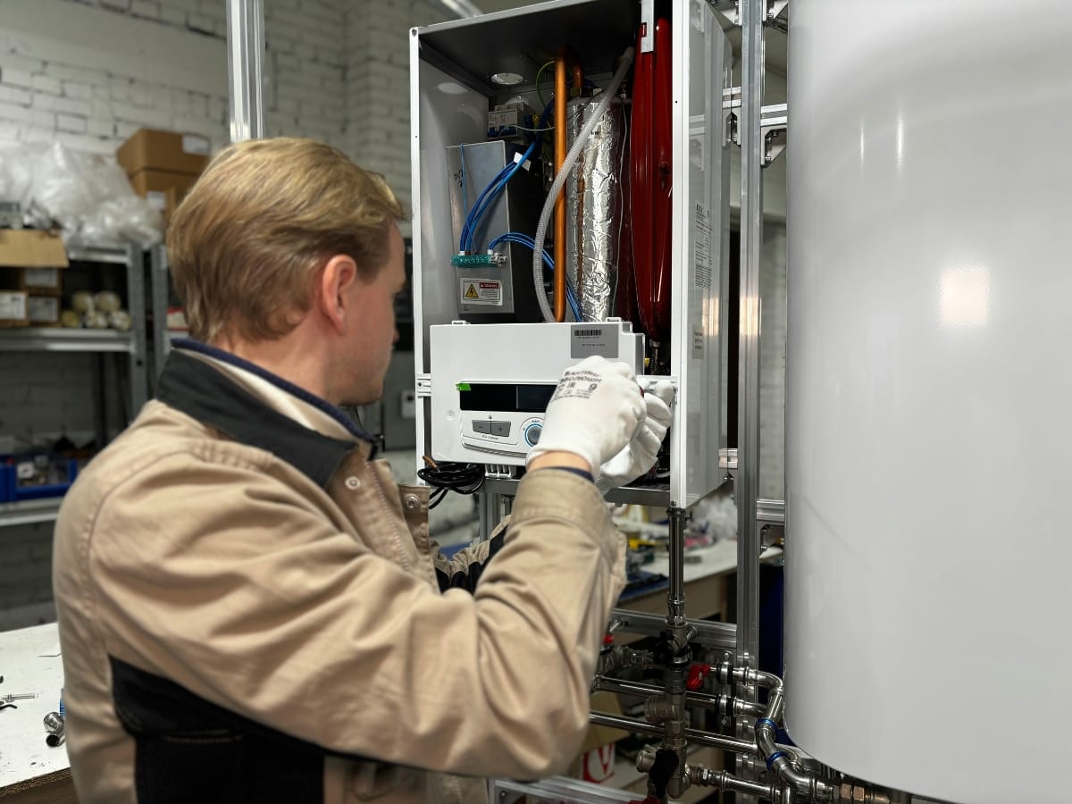 A technician wearing gloves inspects and adjusts controls inside an open electrical panel, ensuring safe and efficient operation as part of comprehensive boiler services in an industrial setting.