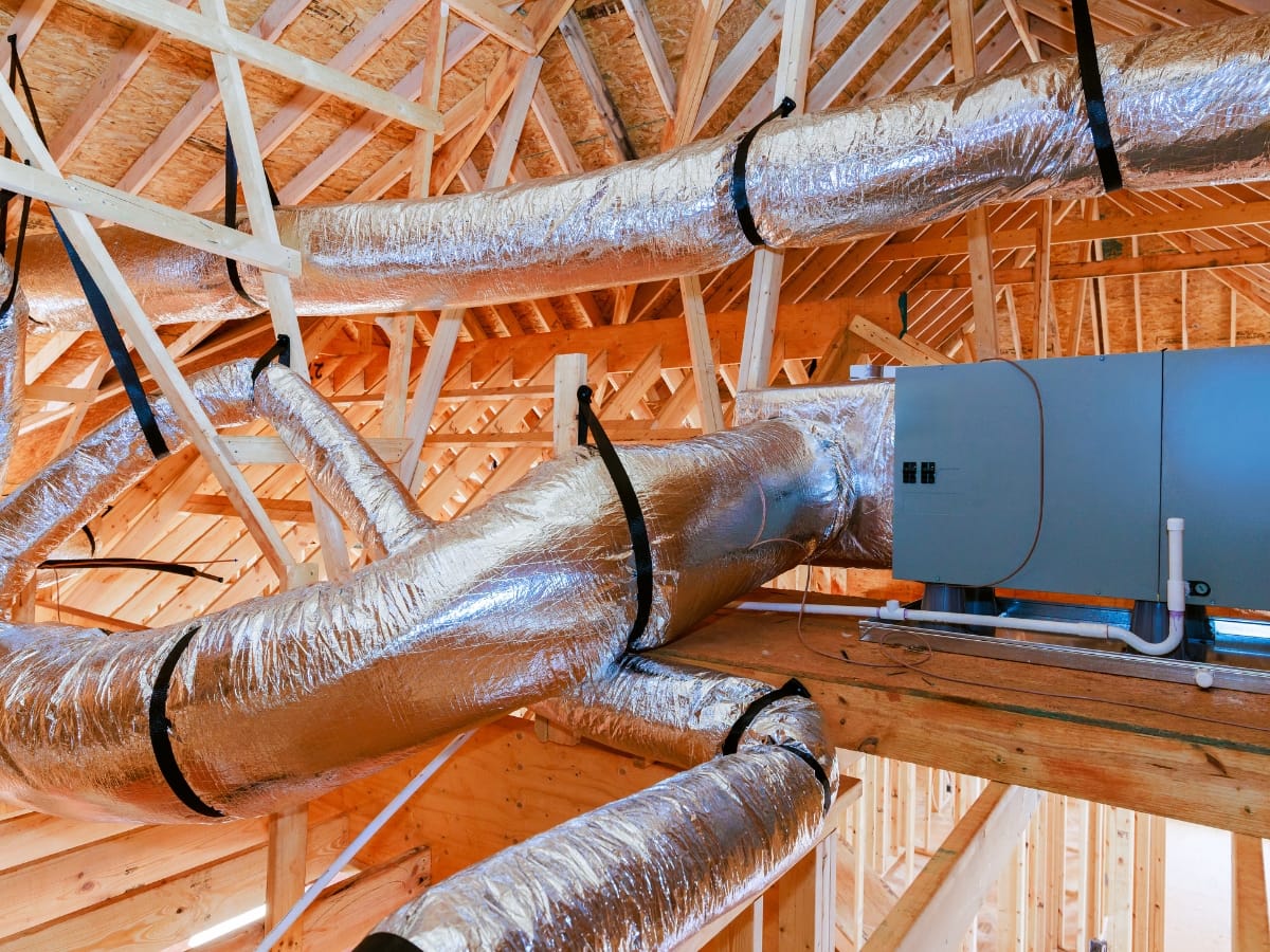 Insulated ductwork and an air handling unit installed in the attic of a building under construction with exposed wooden framing.