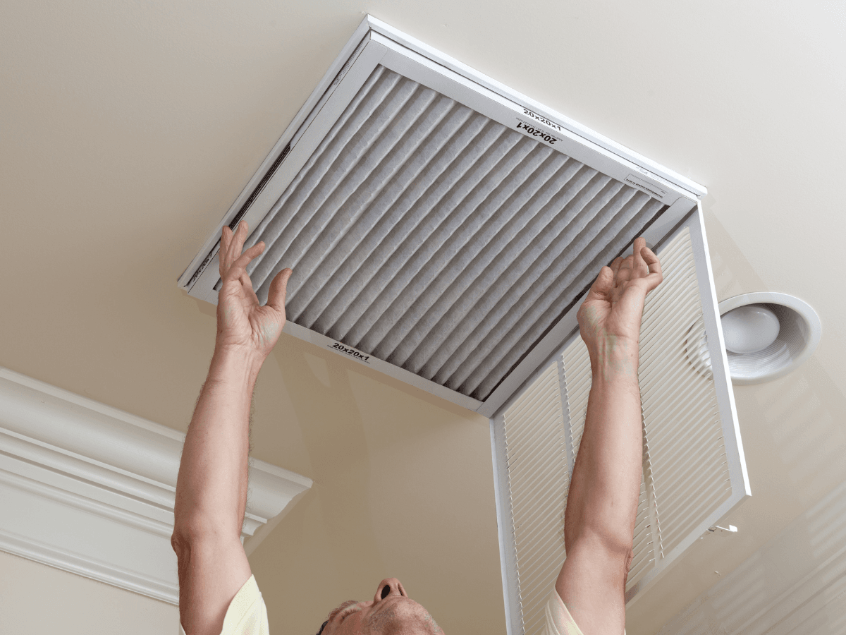 A person installs or replaces furnace filters in a ceiling vent inside a home.