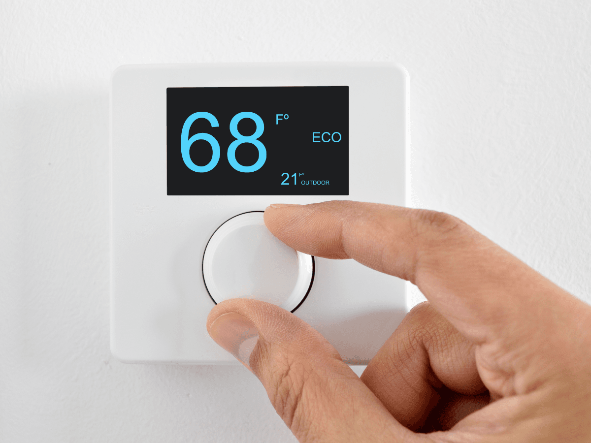 A hand adjusts a digital thermostat set to 68 degrees Fahrenheit on a white wall, with ECO mode and outdoor temperature displayed—an everyday task that can be frustrating if the thermostat is not working properly.
