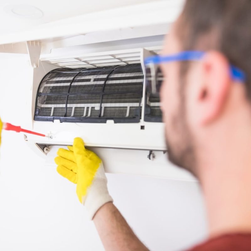 AC Repair Marietta: A person wearing yellow gloves uses a screwdriver to repair or perform AC filter cleaning on a wall-mounted air conditioning unit.