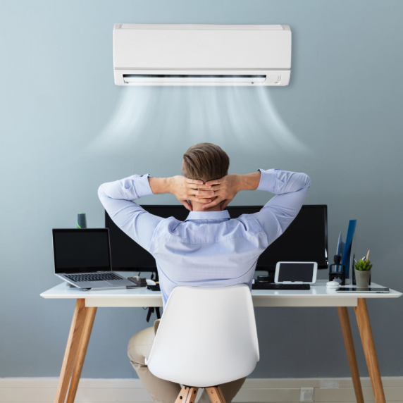 A man sitting at his desk with an air conditioner over his head.