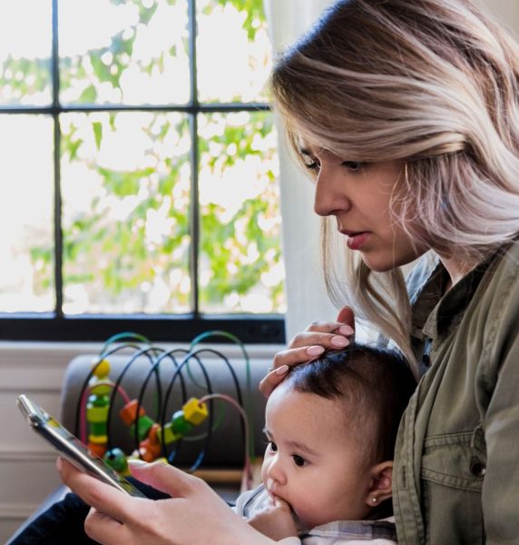 A woman multitasking, holding her baby while she calls Coolpro for Alpharetta hvac services.