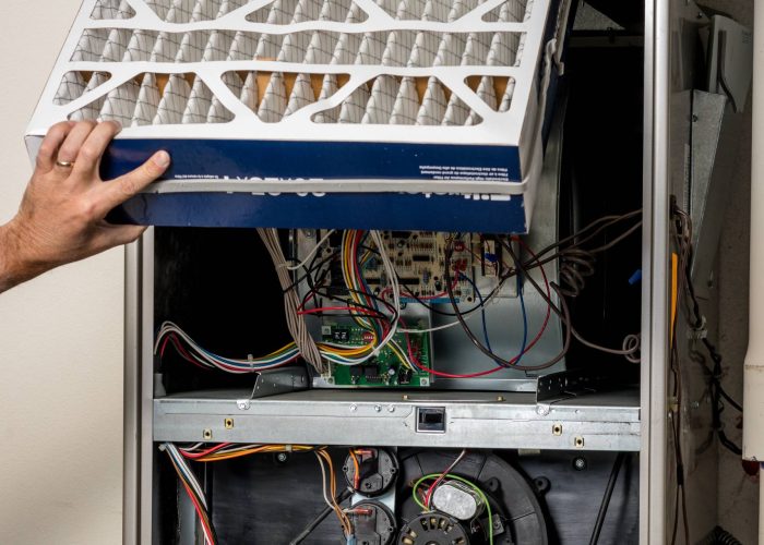 A man performing furnace repair by removing a filter from an air conditioner.