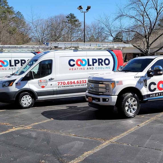 Three white Coolpro Heating and Cooling trucks with their logo branding parked in a parking lot.