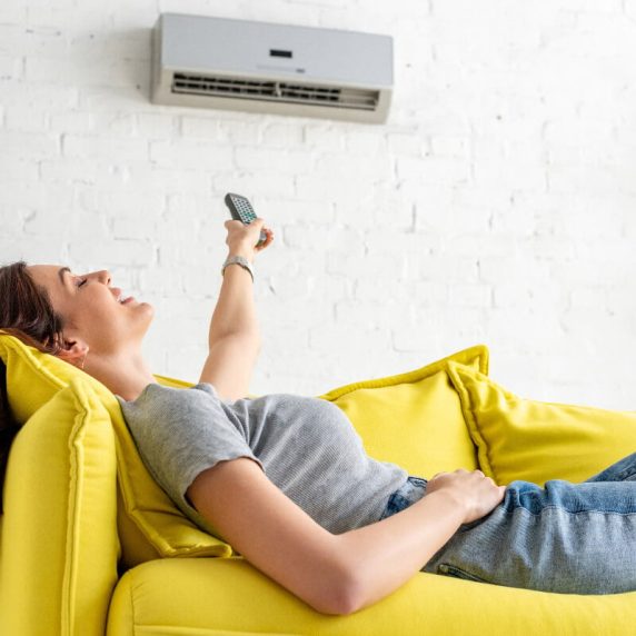 A woman relaxing on a yellow couch with a remote control.